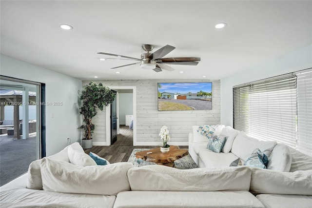 living room with dark wood-type flooring, wood walls, and ceiling fan