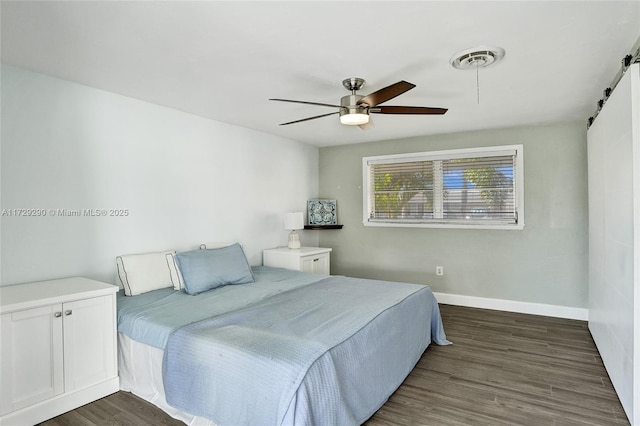 bedroom with ceiling fan, dark wood-type flooring, and a barn door