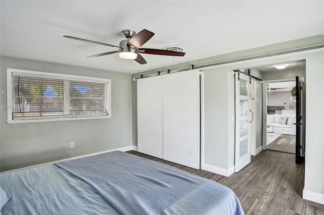 bedroom with ceiling fan, wood-type flooring, and a barn door