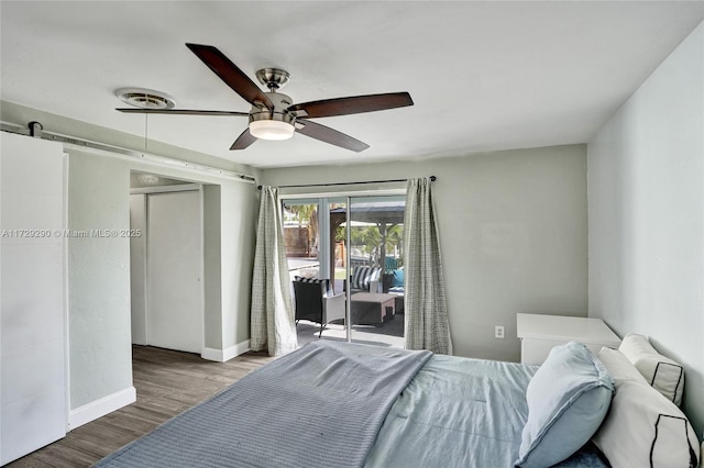 bedroom with ceiling fan, access to exterior, wood-type flooring, and a barn door