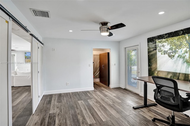 unfurnished office featuring ceiling fan, a barn door, and light hardwood / wood-style flooring