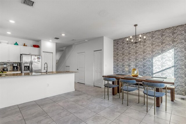 kitchen with light stone countertops, white cabinets, stainless steel refrigerator with ice dispenser, sink, and hanging light fixtures