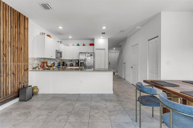 kitchen featuring dark stone countertops, kitchen peninsula, decorative backsplash, white cabinetry, and appliances with stainless steel finishes