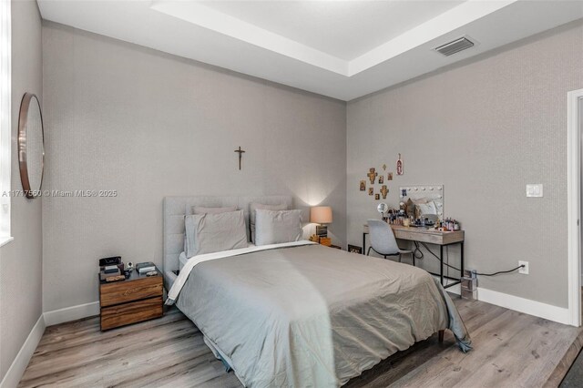 bedroom with light hardwood / wood-style floors and a tray ceiling