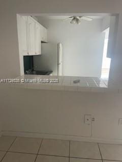 kitchen featuring ceiling fan, tile patterned flooring, white cabinets, and stainless steel fridge