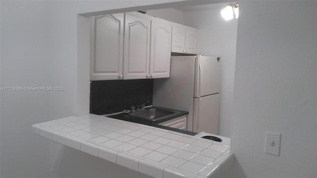 kitchen with white cabinets, white refrigerator, sink, kitchen peninsula, and tile countertops