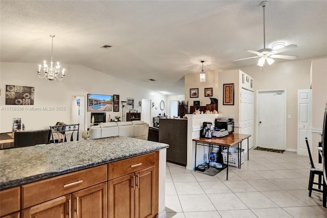 kitchen featuring vaulted ceiling, light tile patterned flooring, stone countertops, ceiling fan with notable chandelier, and decorative light fixtures