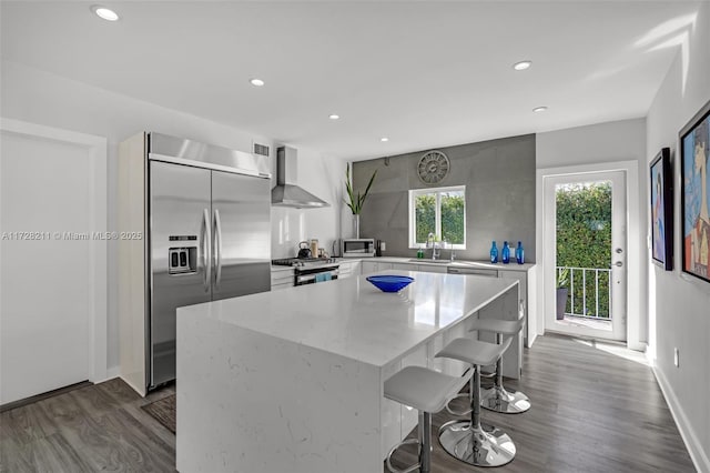 kitchen with modern cabinets, wood finished floors, a center island, stainless steel appliances, and wall chimney range hood
