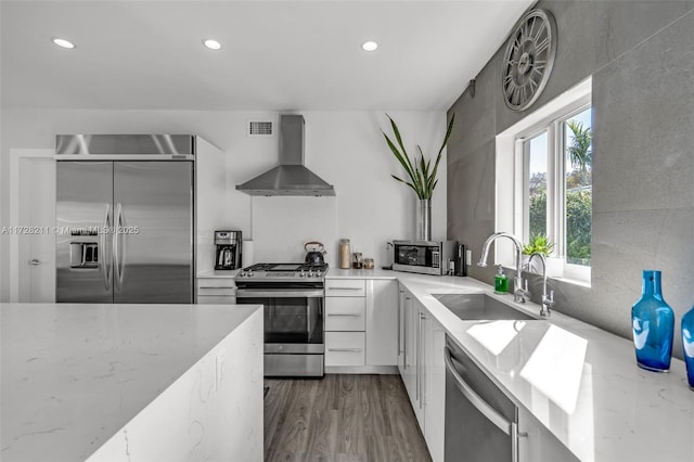 kitchen featuring modern cabinets, appliances with stainless steel finishes, wall chimney range hood, white cabinetry, and a sink