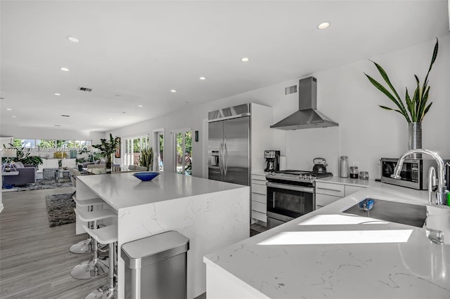 kitchen featuring stainless steel appliances, a sink, visible vents, wall chimney range hood, and modern cabinets