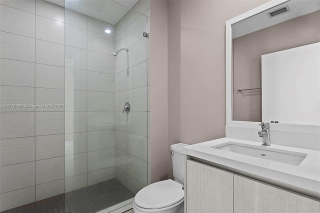 bathroom with toilet, tiled shower, and vanity