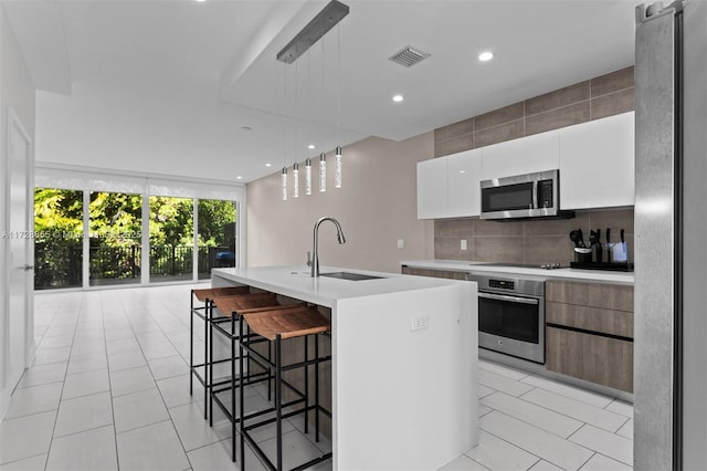 kitchen featuring decorative backsplash, sink, white cabinetry, an island with sink, and stainless steel appliances