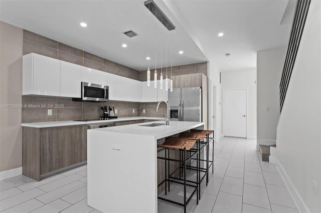 kitchen featuring appliances with stainless steel finishes, white cabinetry, sink, a kitchen breakfast bar, and a kitchen island with sink