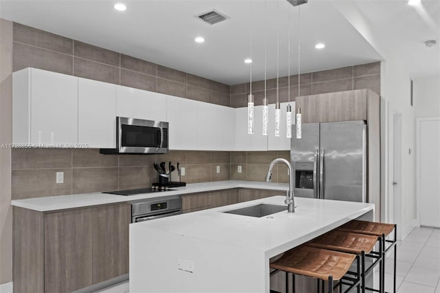 kitchen with pendant lighting, appliances with stainless steel finishes, white cabinets, sink, and a kitchen island with sink