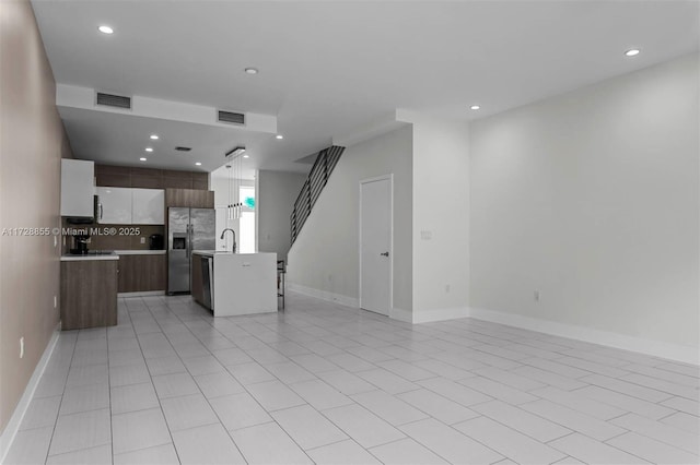 kitchen featuring stainless steel fridge with ice dispenser, an island with sink, decorative backsplash, light tile patterned flooring, and sink