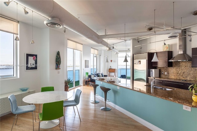 kitchen with sink, hanging light fixtures, wall chimney exhaust hood, and dark stone counters