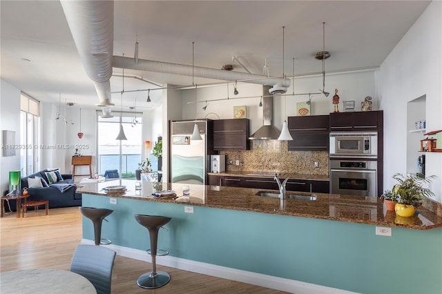 kitchen with sink, stainless steel appliances, wall chimney exhaust hood, and decorative light fixtures