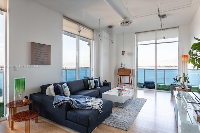 living room featuring light wood-type flooring, floor to ceiling windows, and a water view