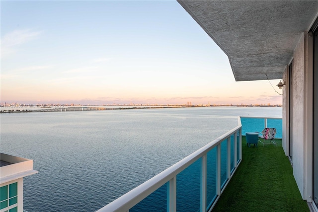 balcony at dusk featuring a water view