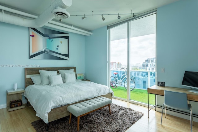 bedroom with expansive windows, rail lighting, access to outside, hardwood / wood-style floors, and a baseboard heating unit