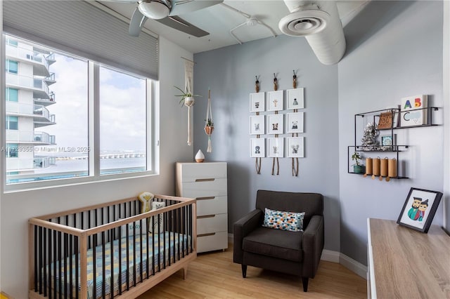 bedroom with a crib, ceiling fan, and light hardwood / wood-style flooring