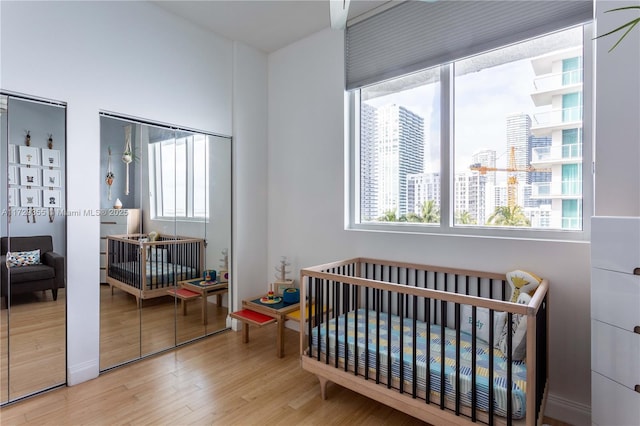 bedroom with multiple windows, light wood-type flooring, a nursery area, and two closets