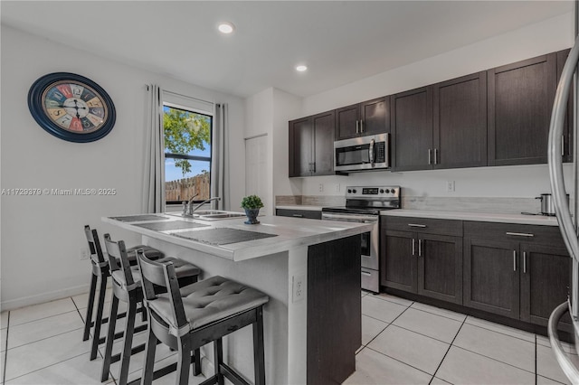 kitchen with a kitchen bar, a center island with sink, stainless steel appliances, light tile patterned flooring, and sink