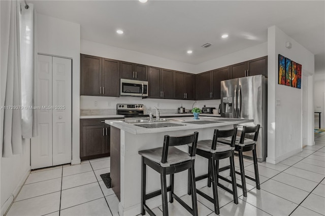 kitchen with a breakfast bar area, appliances with stainless steel finishes, a center island with sink, and dark brown cabinetry