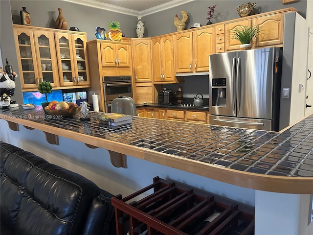 kitchen with stainless steel appliances, tile counters, ornamental molding, a kitchen bar, and kitchen peninsula