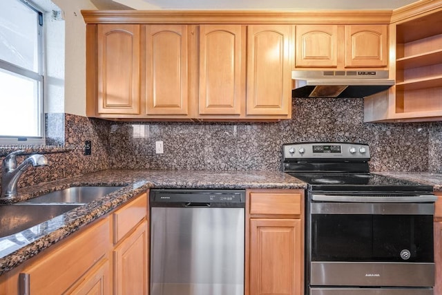 kitchen with dark stone counters, decorative backsplash, stainless steel appliances, under cabinet range hood, and a sink