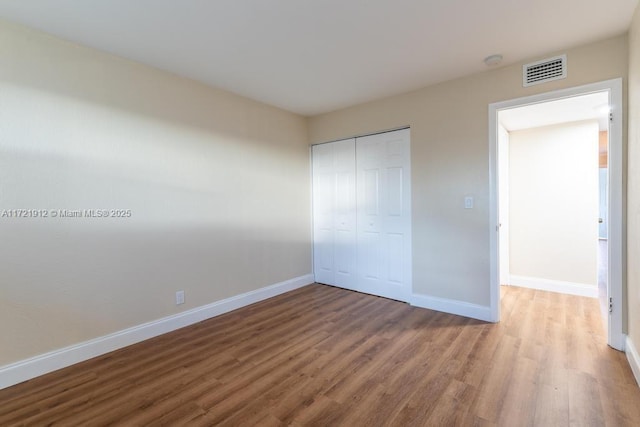 unfurnished bedroom with baseboards, a closet, visible vents, and wood finished floors