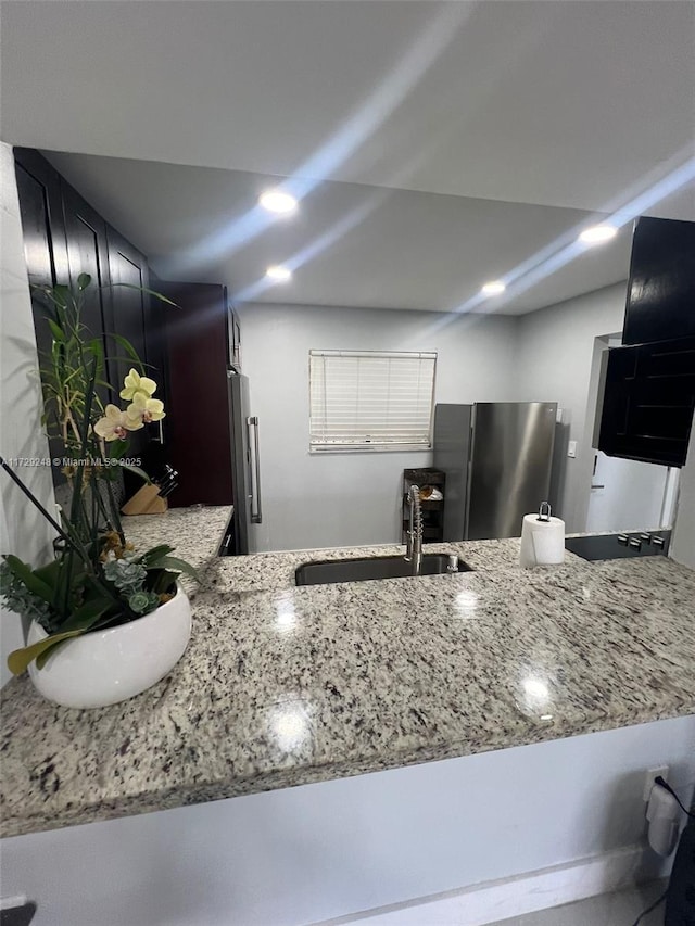 kitchen featuring kitchen peninsula, stainless steel fridge, light stone counters, and sink