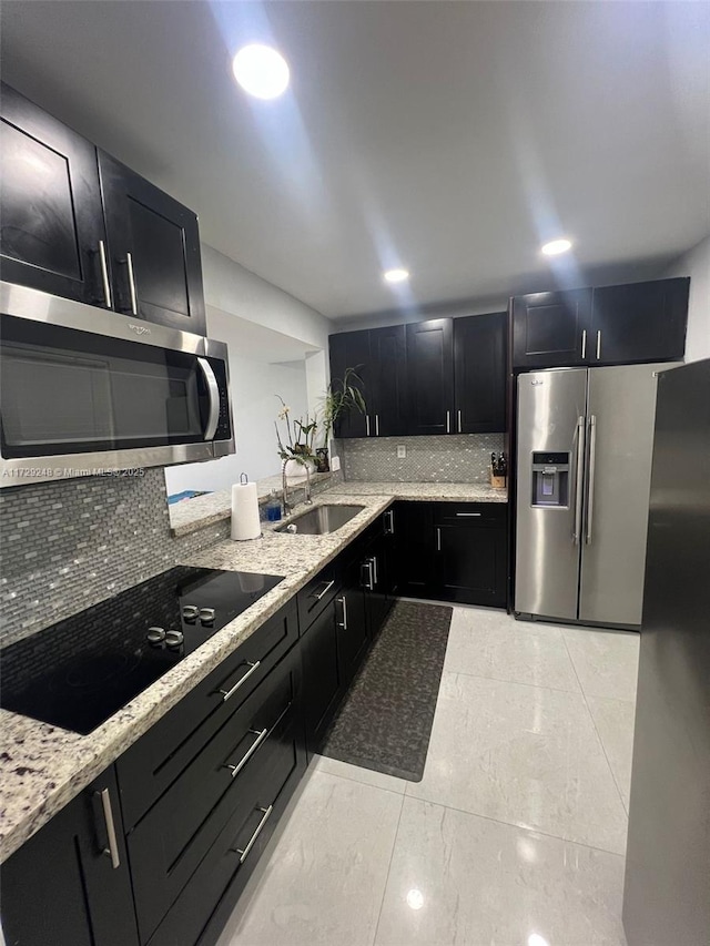 kitchen featuring tasteful backsplash, light stone countertops, appliances with stainless steel finishes, and sink