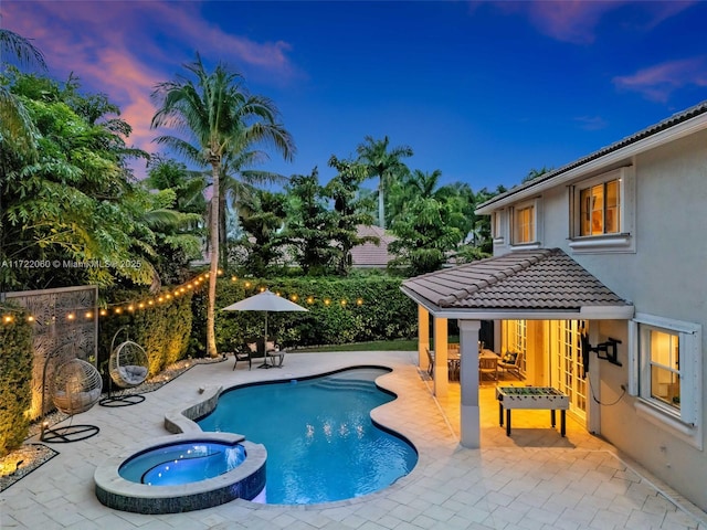 pool at dusk featuring a patio area and an in ground hot tub