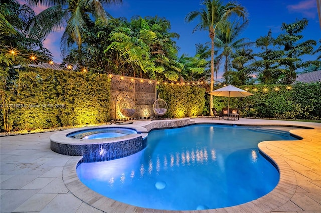 pool at dusk with a patio area and an in ground hot tub