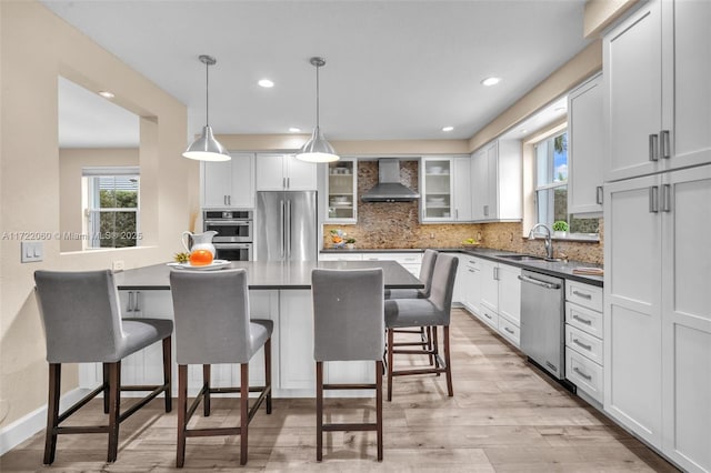 kitchen featuring pendant lighting, wall chimney range hood, appliances with stainless steel finishes, and white cabinetry