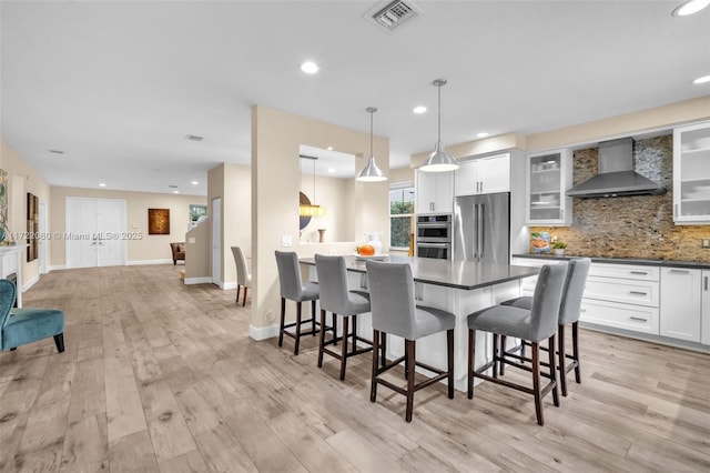 kitchen with tasteful backsplash, wall chimney range hood, pendant lighting, white cabinetry, and appliances with stainless steel finishes