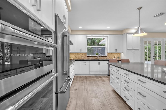 kitchen with white cabinetry, stainless steel appliances, decorative light fixtures, and sink