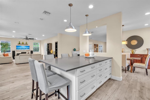 kitchen with a kitchen breakfast bar, pendant lighting, white cabinets, and light wood-type flooring