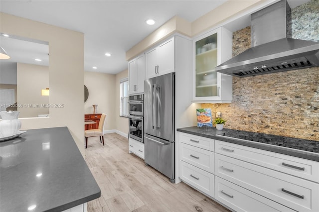 kitchen with tasteful backsplash, light wood-type flooring, appliances with stainless steel finishes, white cabinets, and wall chimney exhaust hood