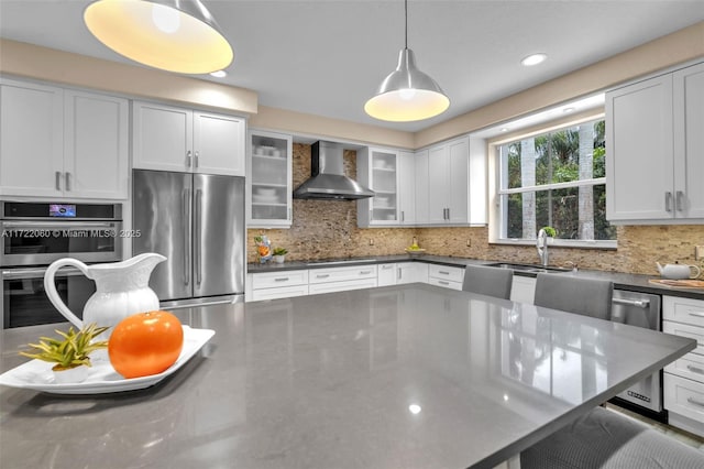 kitchen featuring decorative light fixtures, backsplash, white cabinetry, stainless steel appliances, and wall chimney exhaust hood