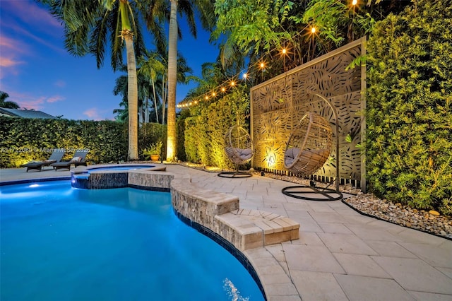 pool at dusk featuring a patio area and an in ground hot tub