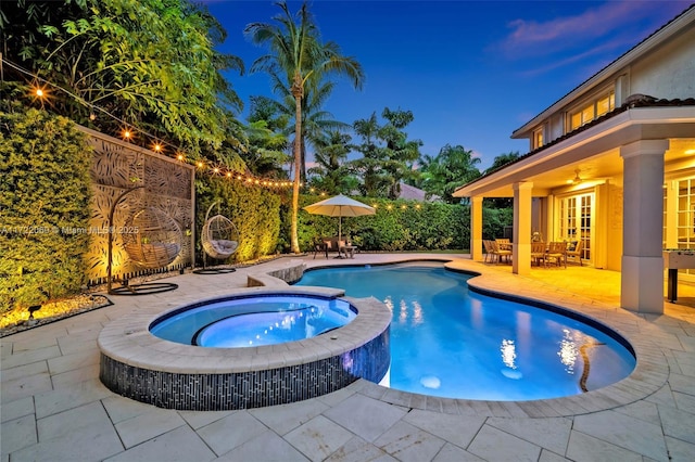 pool at dusk featuring ceiling fan, a patio area, and an in ground hot tub