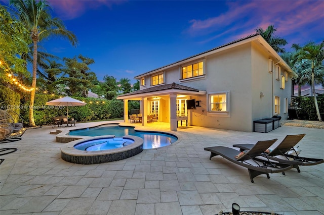 back house at dusk featuring a swimming pool with hot tub and a patio