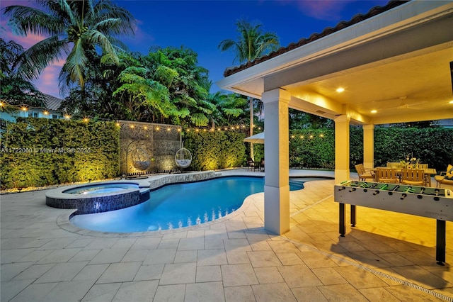 pool at dusk with a patio and an in ground hot tub