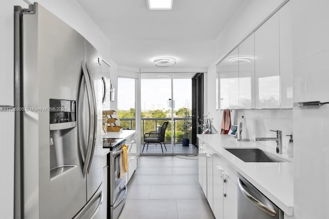 kitchen with sink, white cabinets, light tile patterned floors, and stainless steel appliances