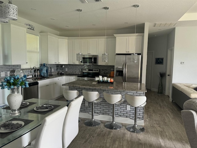 kitchen featuring decorative light fixtures, a breakfast bar, sink, white cabinetry, and stainless steel appliances