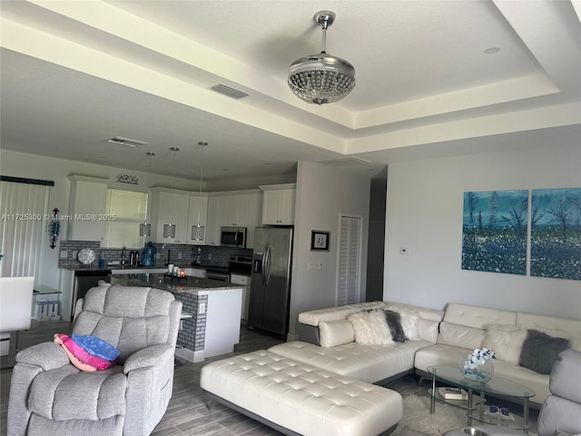 living room with a raised ceiling, sink, and hardwood / wood-style floors