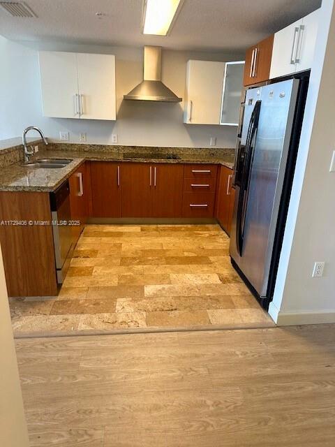 kitchen featuring appliances with stainless steel finishes, wall chimney exhaust hood, white cabinetry, dark stone countertops, and sink