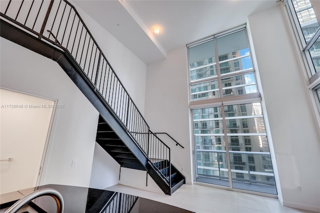 stairs with tile patterned floors, floor to ceiling windows, and a high ceiling